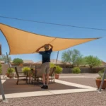 Person installing a triangular sun sail over a patio in a Southeast Valley backyard